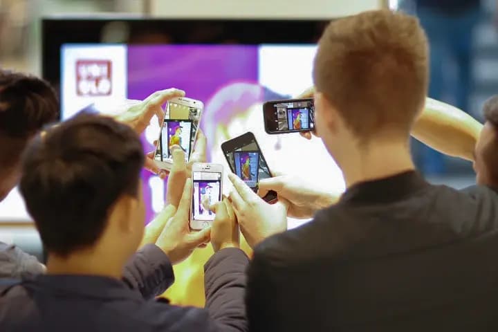 Four people using their phones to take pictures of a QR code on a UNIQLO promotional screen.