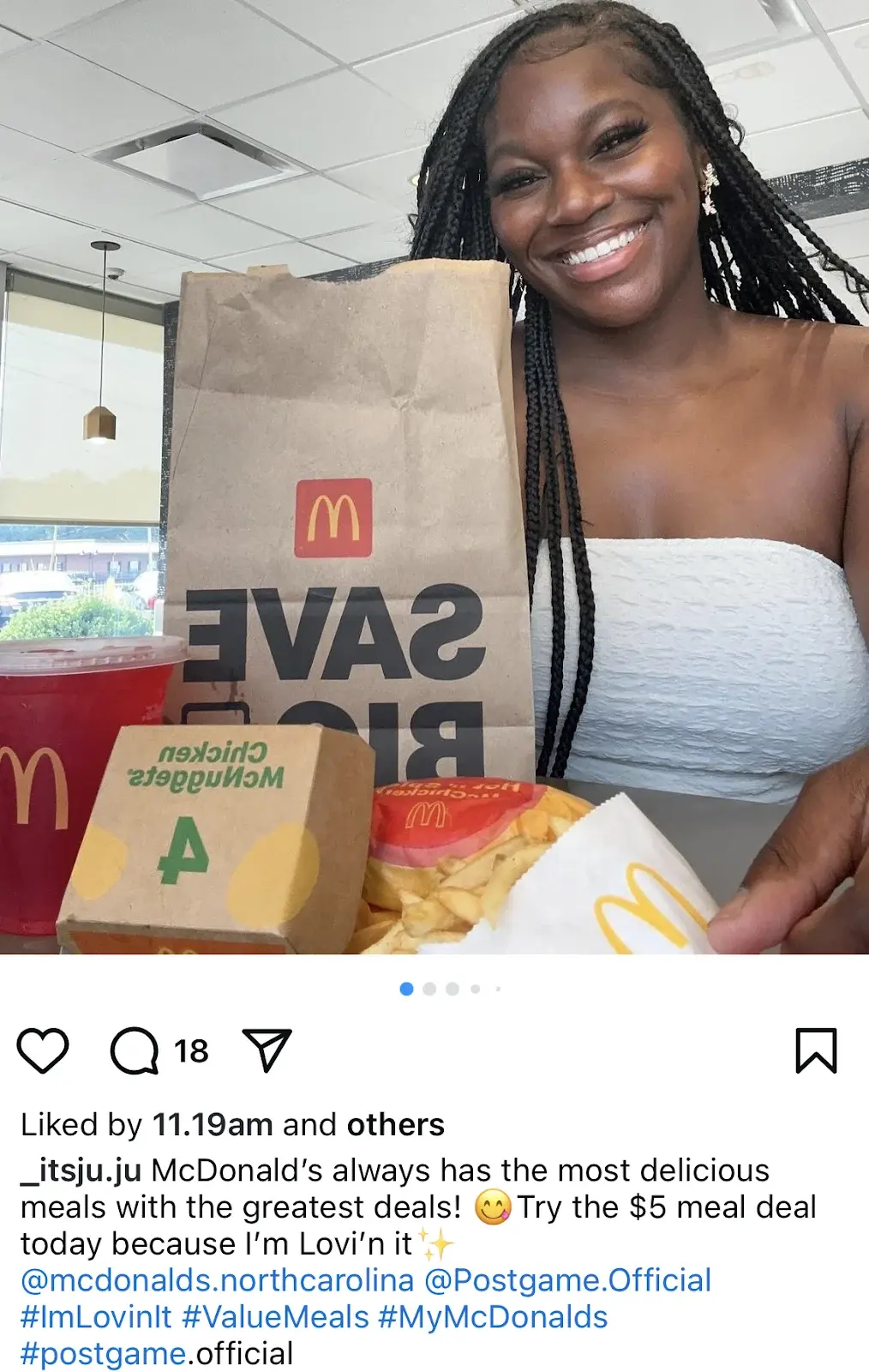 A woman smiles at a table with a McDonalds paper bag, fries, a drink, and a box of Chicken McNuggets.