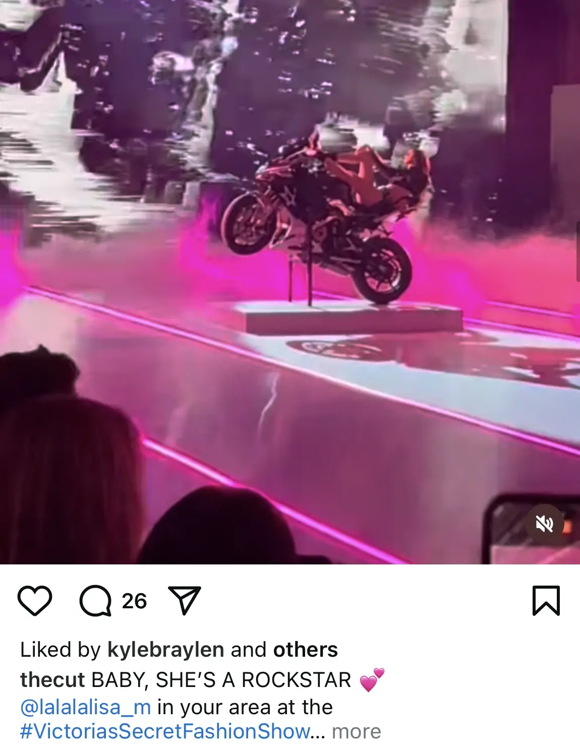 A motorcycle is displayed on stage with pink lights and smoke effects at a fashion show event.